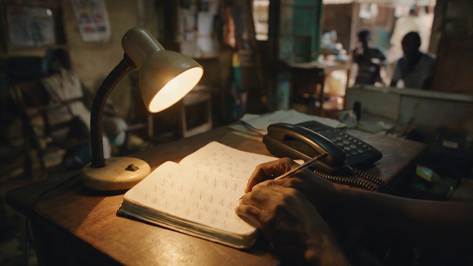 A week of calls tallied by hand in a notebook, beside the desk phone, under a lamp at night